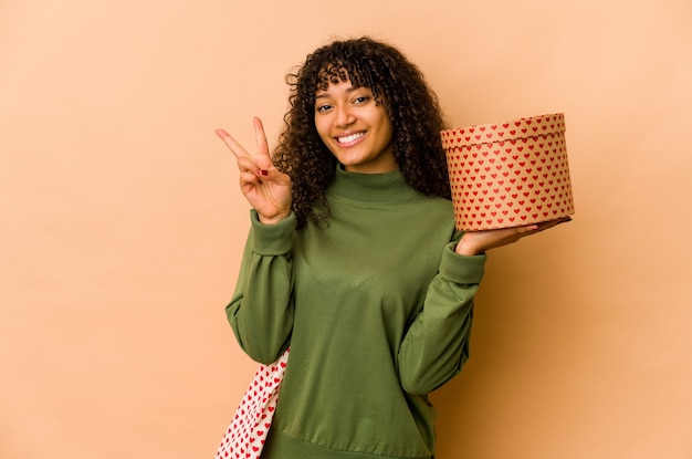 Joven afroamericana afro sosteniendo un regalo de San Valentín mostrando el número dos con los dedos.