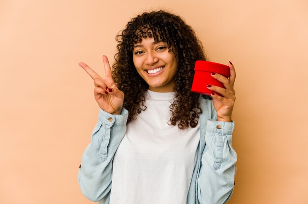 Joven afroamericana afro sosteniendo un regalo de San Valentín mostrando el número dos con los dedos.