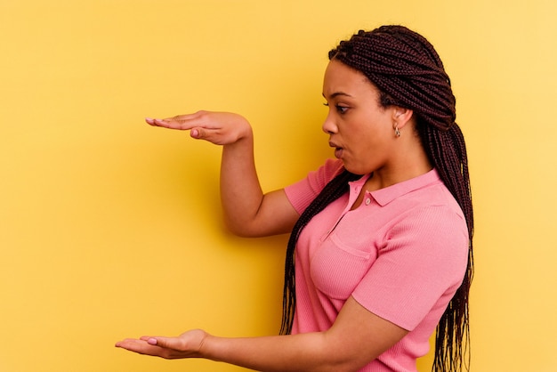 Joven afroamericana aislada en amarillo sorprendido y sorprendido sosteniendo un espacio de copia entre las manos.
