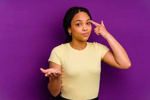 Joven afroamericana aislada en amarillo sosteniendo y mostrando un producto en la mano.