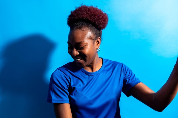 Joven afroamericana aislada en un estudio de fondo azul sonriendo y bailando