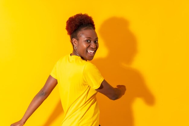 Joven afroamericana aislada en un fondo amarillo sonriendo y bailando en una sesión de estudio