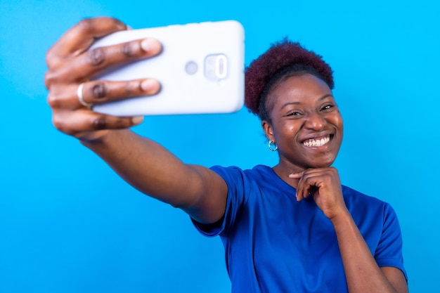 Joven afroamericana aislada en un fondo azul sonriendo y haciendo una sesión de estudio selfie