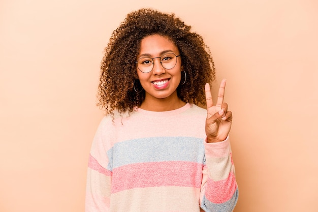 Joven afroamericana aislada de fondo beige alegre y despreocupada mostrando un símbolo de paz con los dedos