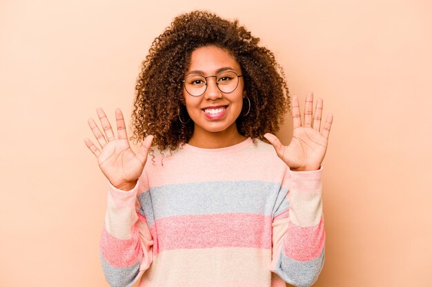 Joven afroamericana aislada de fondo beige que muestra el número diez con las manos