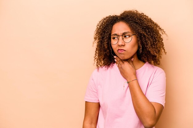 Joven afroamericana aislada de fondo beige tocando la parte posterior de la cabeza pensando y tomando una decisión