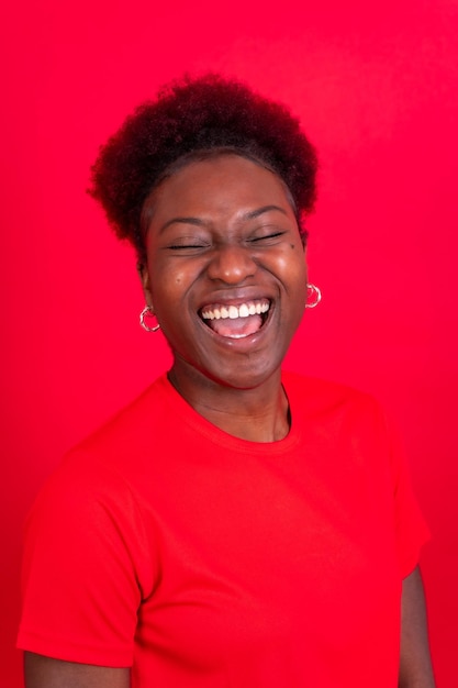 Joven afroamericana aislada en un fondo rojo sonriendo y riendo en una sesión de estudio