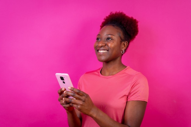 Joven afroamericana aislada en un fondo rosado sonriendo con la sesión de estudio del teléfono móvil