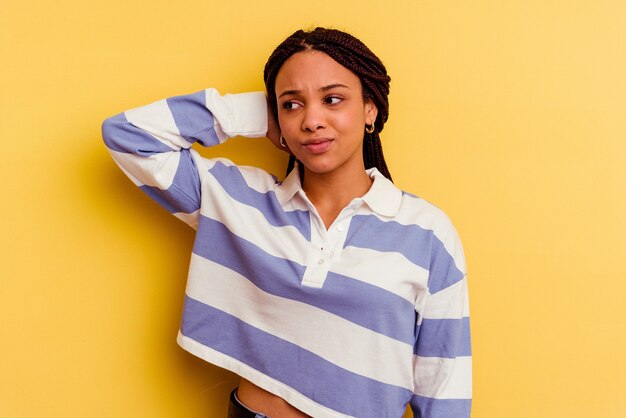 Joven afroamericana aislada en la pared amarilla cansada y con mucho sueño manteniendo la mano en la cabeza.