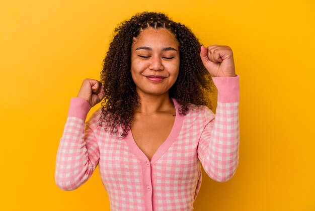 Joven afroamericana aislada en la pared amarilla celebrando una victoria, pasión y entusiasmo, expresión feliz.