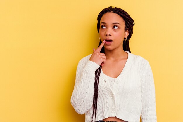 Joven afroamericana aislada en la pared amarilla mirando hacia los lados con expresión dudosa y escéptica.