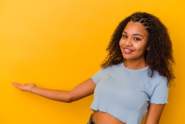 Joven afroamericana aislada en la pared amarilla mostrando algo en el espacio de la copia