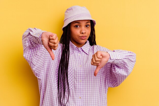 Joven afroamericana aislada en la pared amarilla que muestra el pulgar hacia abajo, el concepto de decepción.