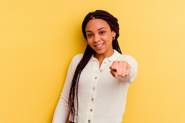 Joven afroamericana aislada en la pared amarilla sonrisas alegres apuntando al frente