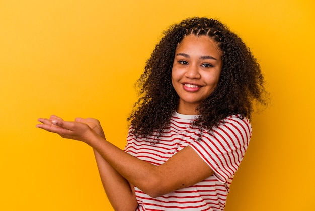 Joven afroamericana aislada en la pared amarilla sosteniendo un espacio de copia en una palma