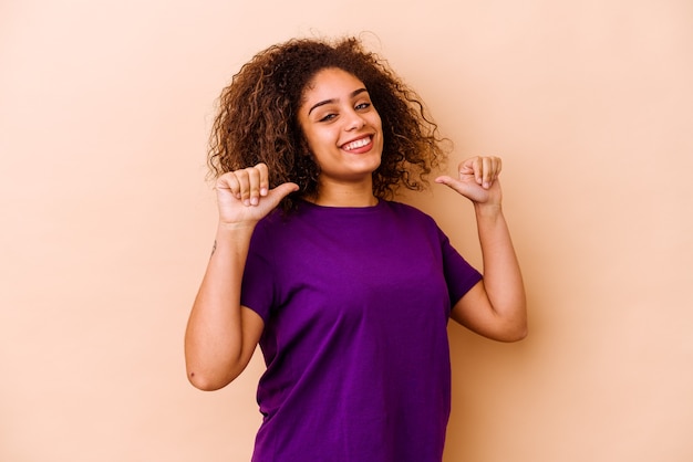 Joven afroamericana aislada en la pared beige se siente orgullosa y segura de sí misma, ejemplo a seguir.