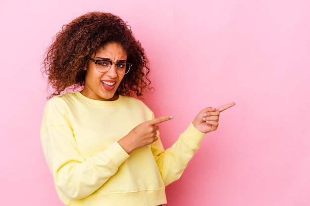 Joven afroamericana aislada en la pared rosa apuntando con los dedos índices a un espacio de copia, expresando entusiasmo y deseo