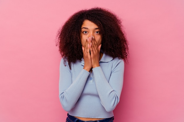 Joven afroamericana aislada en la pared rosa conmocionada, cubriendo la boca con las manos, ansiosa por descubrir algo nuevo.