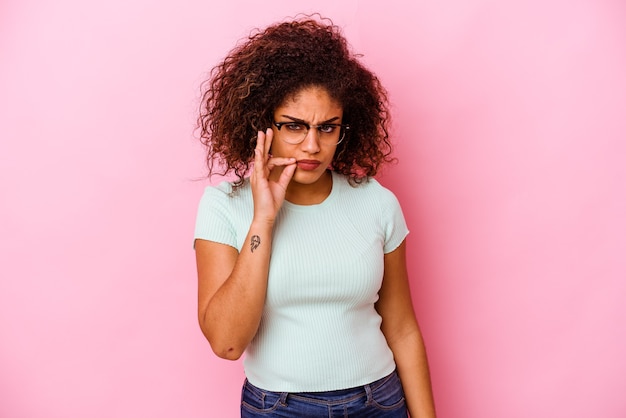 Joven afroamericana aislada en la pared rosa con los dedos en los labios guardando un secreto