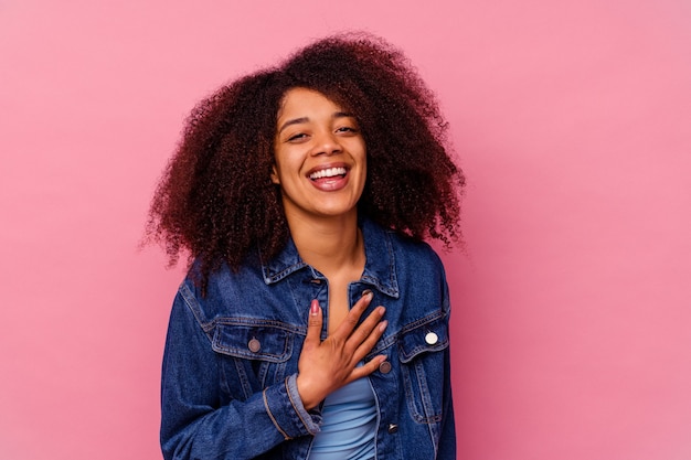 Joven afroamericana aislada en la pared rosa se ríe a carcajadas manteniendo la mano en el pecho.