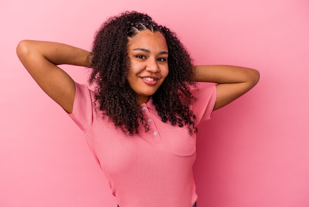 Joven afroamericana aislada en la pared rosa sintiéndose confiada, con las manos detrás de la cabeza