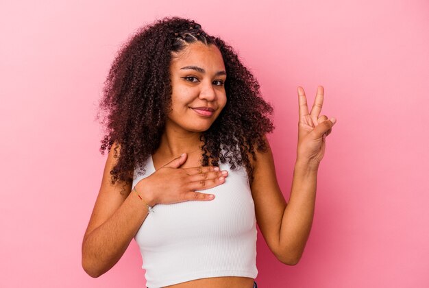 Joven afroamericana aislada en la pared rosa tomando un juramento, poniendo la mano en el pecho.