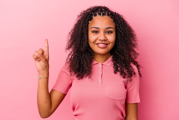 Joven afroamericana aislada en la pared rosada mostrando el número uno con el dedo