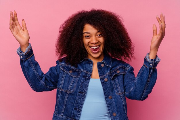 Joven afroamericana aislada en rosa celebrando una victoria o un éxito, está sorprendido y consternado.