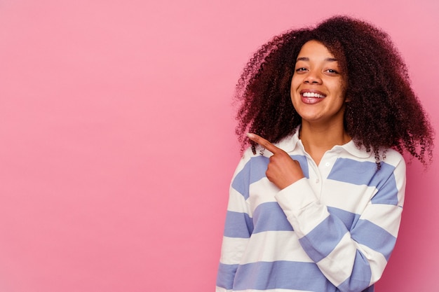 Joven afroamericana aislada en rosa sonriendo y apuntando a un lado, mostrando algo en el espacio en blanco.