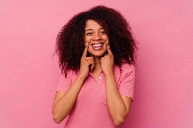 Joven afroamericana aislada en rosa sonrisas, señalando con el dedo a la boca.