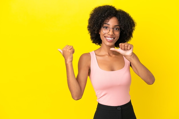 Joven afroamericana aislada sobre fondo amarillo apuntando hacia el lado para presentar un producto