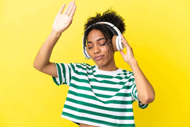 Joven afroamericana aislada sobre fondo amarillo escuchando música y bailando