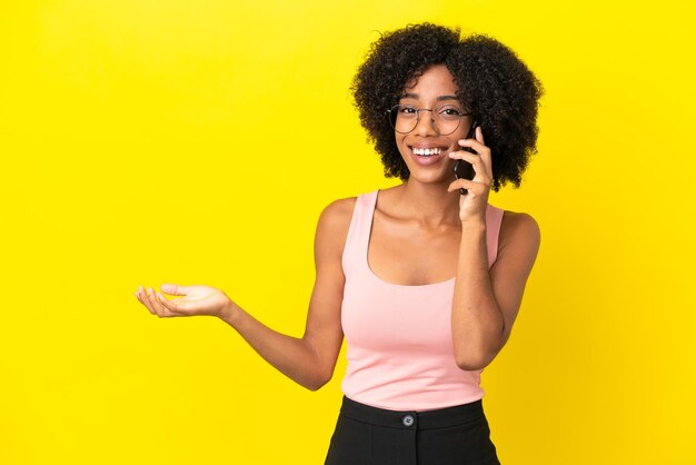 Joven afroamericana aislada sobre fondo amarillo manteniendo una conversación con el teléfono móvil con alguien