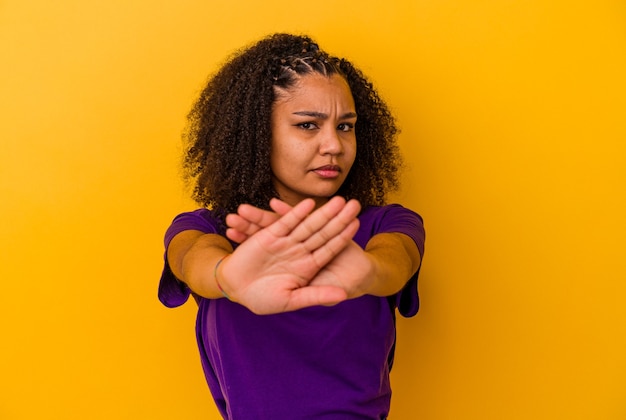 Joven afroamericana aislada sobre fondo amarillo de pie con la mano extendida mostrando la señal de stop, impidiéndote.