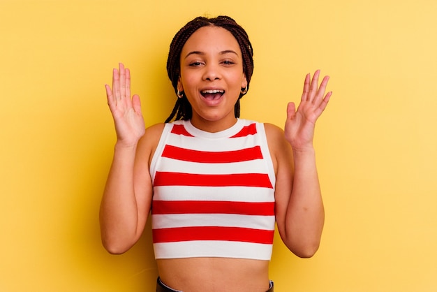 Joven afroamericana aislada sobre fondo amarillo se ríe a carcajadas manteniendo la mano en el pecho.