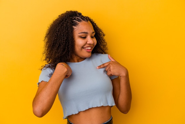 Joven afroamericana aislada sobre fondo amarillo sorprendió señalando con el dedo, sonriendo ampliamente.