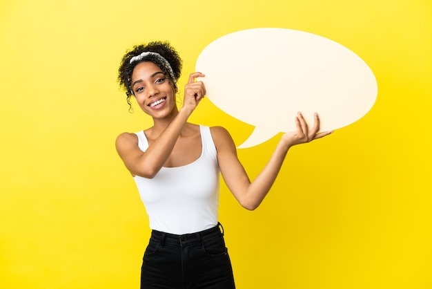 Joven afroamericana aislada sobre fondo amarillo sosteniendo un bocadillo de diálogo vacío