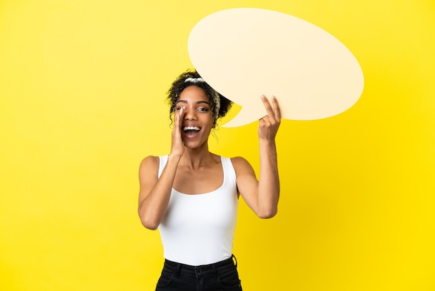 Joven afroamericana aislada sobre fondo amarillo sosteniendo un bocadillo vacío y gritando