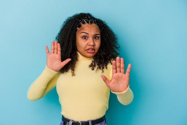 Joven afroamericana aislada sobre fondo azul conmocionada debido a un peligro inminente