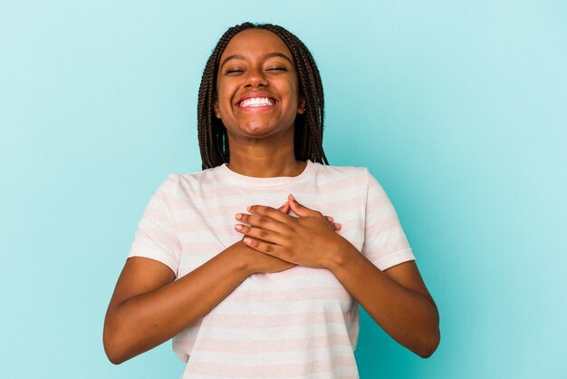 Joven afroamericana aislada sobre fondo azul riendo manteniendo las manos en el corazón, concepto de felicidad.