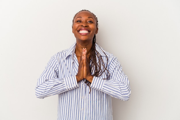 Joven afroamericana aislada sobre fondo blanco tomados de la mano en oración cerca de la boca, se siente confiada.