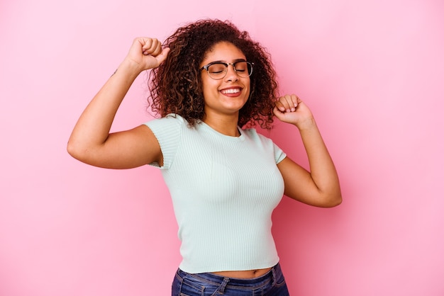 Joven afroamericana aislada sobre fondo rosa celebrando un día especial, salta y levanta los brazos con energía.