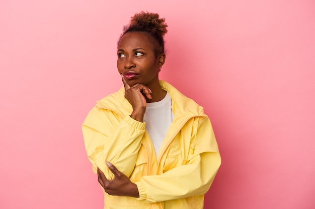 Joven afroamericana aislada sobre fondo rosa contemplando, planificando una estrategia, pensando en la forma de un negocio.