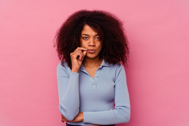 Joven afroamericana aislada sobre fondo rosa con los dedos en los labios guardando un secreto.