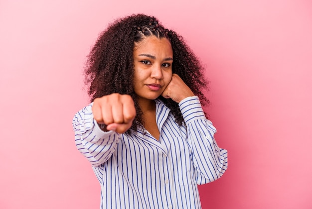 Joven afroamericana aislada sobre fondo rosa lanzando un puñetazo, ira, luchando debido a una discusión, boxeo.