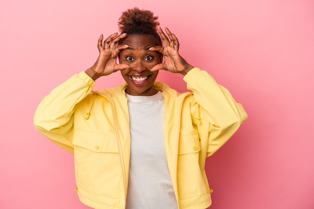 Joven afroamericana aislada sobre fondo rosa manteniendo los ojos abiertos para encontrar una oportunidad de éxito.