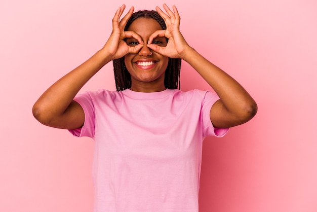 Joven afroamericana aislada sobre fondo rosa mostrando bien firmar sobre los ojos