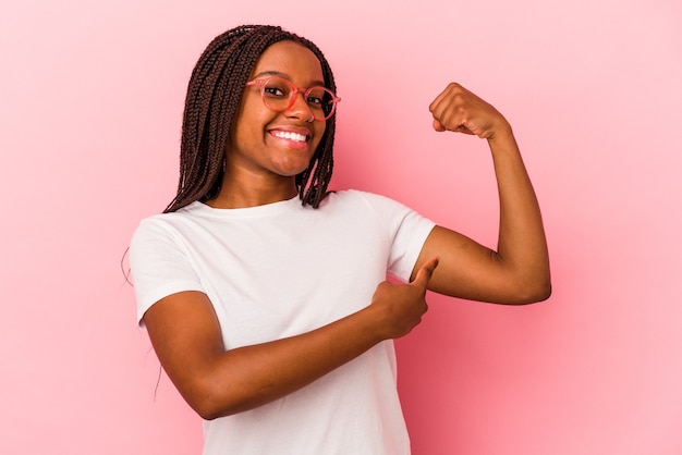 Joven afroamericana aislada sobre fondo rosa mostrando gesto de fuerza con los brazos, símbolo del poder femenino