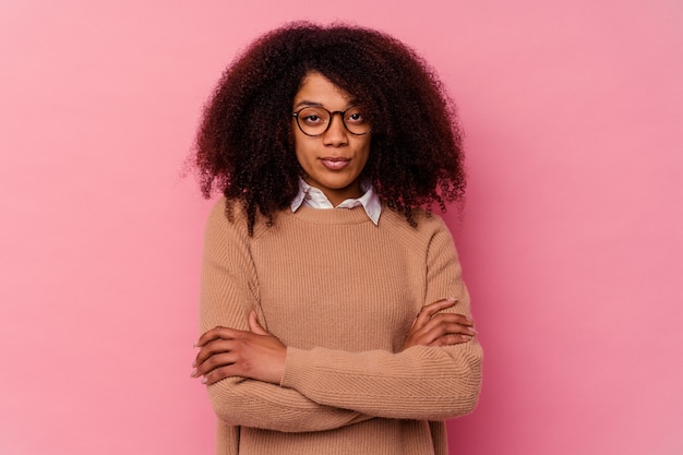 Joven afroamericana aislada sobre fondo rosa que se siente segura, cruzando los brazos con determinación.