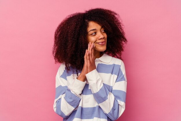 Joven afroamericana aislada sobre fondo rosa rezando, mostrando devoción, persona religiosa en busca de inspiración divina.